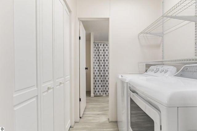 laundry area featuring washing machine and clothes dryer, light wood-style flooring, and baseboards