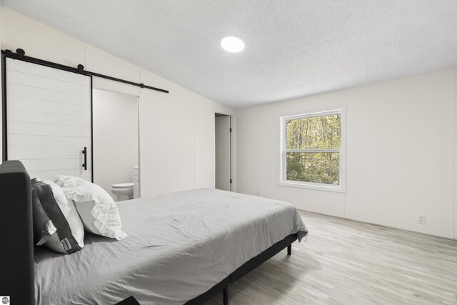 bedroom featuring a barn door, wood finished floors, a textured ceiling, and lofted ceiling