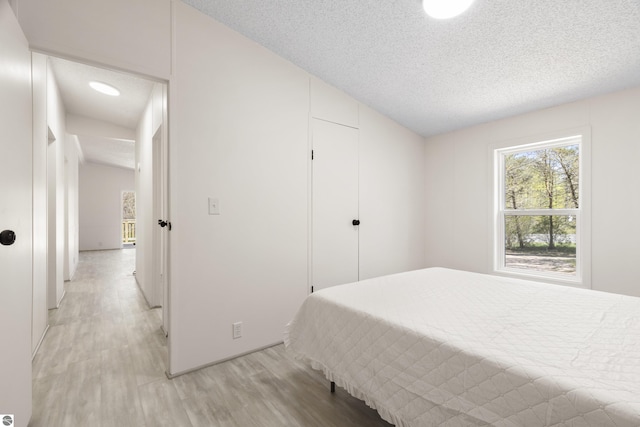 bedroom featuring light wood-type flooring, a textured ceiling, a closet, and vaulted ceiling