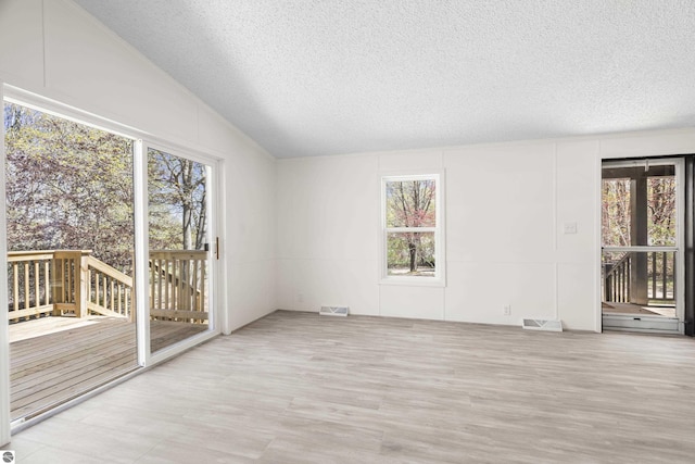 spare room with a textured ceiling, plenty of natural light, wood finished floors, and lofted ceiling