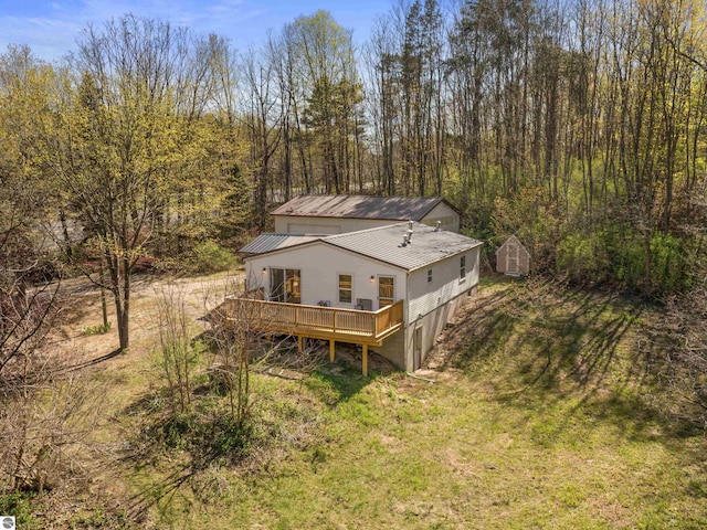 rear view of property featuring a wooden deck, metal roof, a storage shed, an outdoor structure, and a forest view