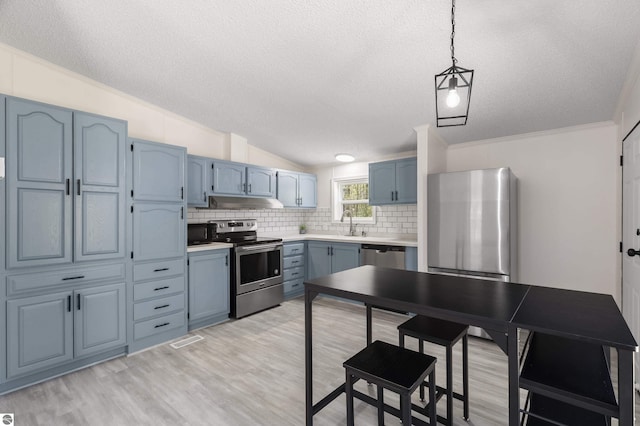 kitchen with appliances with stainless steel finishes, a textured ceiling, blue cabinetry, tasteful backsplash, and light wood finished floors