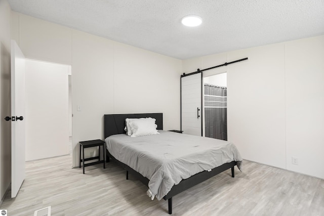 bedroom with a barn door, light wood finished floors, and a textured ceiling