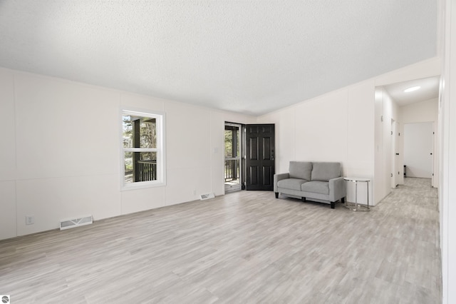 unfurnished room with light wood finished floors, a textured ceiling, and lofted ceiling