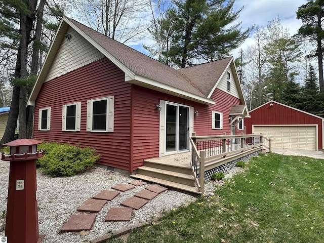 view of front facade featuring a garage, an outbuilding, roof with shingles, a wooden deck, and a front yard