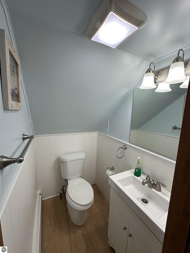half bathroom featuring a baseboard radiator, wood finished floors, wainscoting, toilet, and vanity