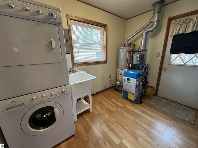 laundry area featuring stacked washing machine and dryer, gas water heater, light wood-type flooring, and healthy amount of natural light