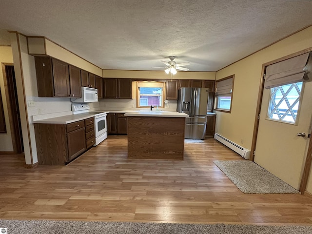 kitchen with white appliances, baseboard heating, a sink, a textured ceiling, and light wood-type flooring