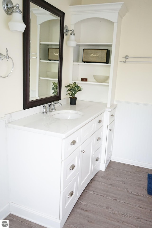 bathroom with a wainscoted wall, vanity, and wood finished floors