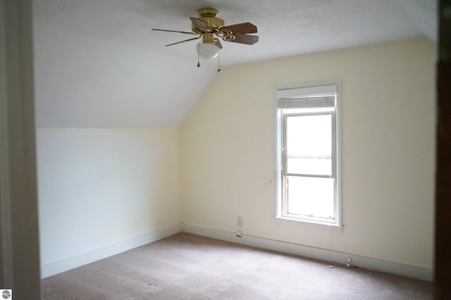 additional living space featuring healthy amount of natural light, light colored carpet, vaulted ceiling, and a ceiling fan