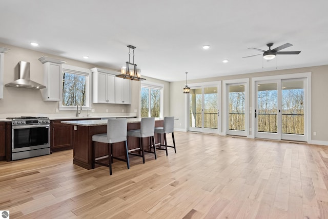 3046 E Greenwood Rd, Lake Leelanau, MI 49653 - kitchen with wall chimney exhaust hood, stainless steel range with gas stovetop, light wood finished floors, a center island, and a breakfast bar
