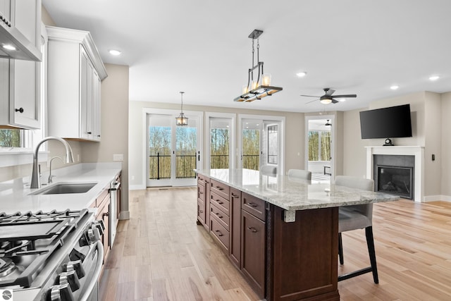 3046 E Greenwood Rd, Lake Leelanau, MI 49653 - kitchen featuring a sink, light wood-style flooring, a ceiling fan, stainless steel range with gas stovetop, and a kitchen bar