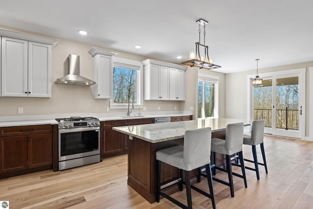 3046 E Greenwood Rd, Lake Leelanau, MI 49653 - kitchen featuring wall chimney range hood, stainless steel appliances, a sink, a breakfast bar area, and light wood-style floors