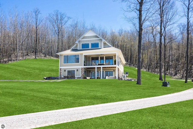 3046 E Greenwood Rd, Lake Leelanau, MI 49653 - back of property with stone siding, a yard, a ceiling fan, a wooded view, and a balcony