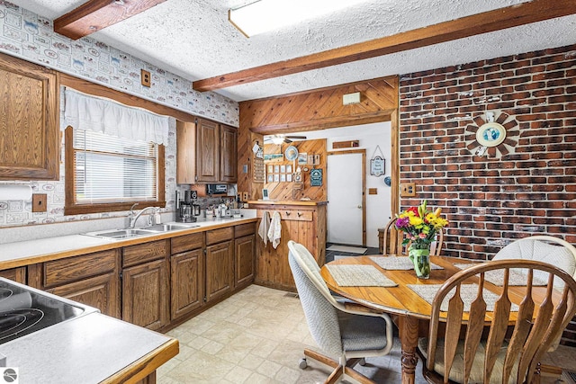 kitchen featuring beamed ceiling, a sink, light countertops, wooden walls, and brown cabinetry