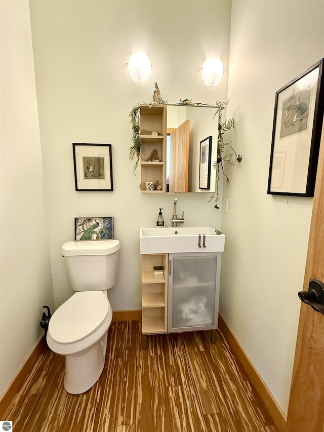 half bathroom with toilet, wood finished floors, baseboards, and a sink