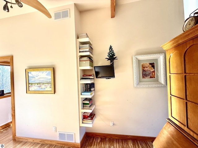 hallway featuring baseboards, beam ceiling, and wood finished floors