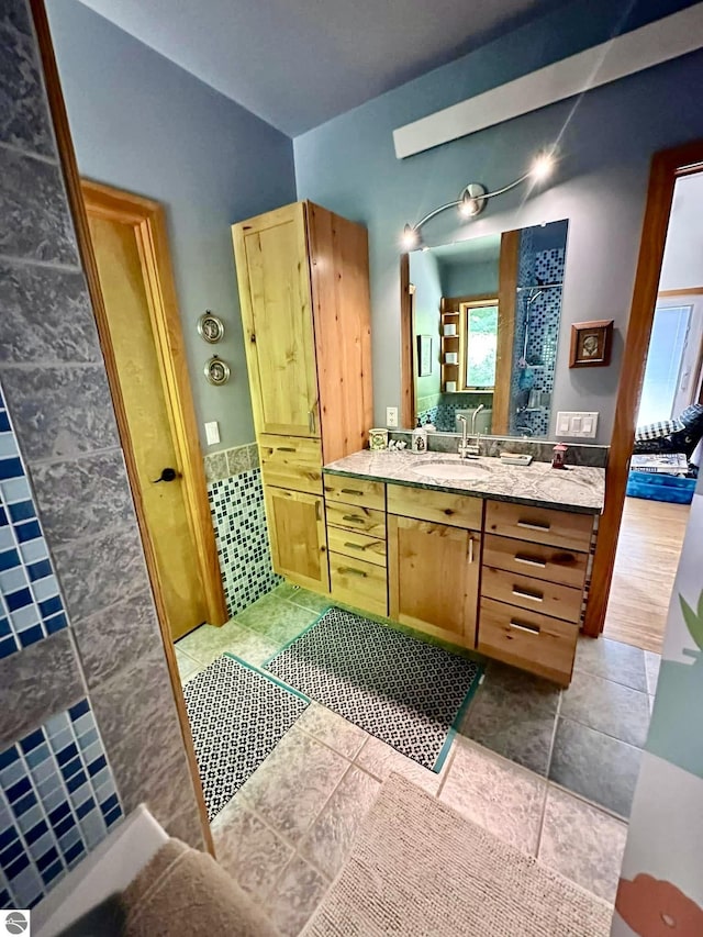 full bath featuring tiled shower, vanity, tile walls, and wainscoting