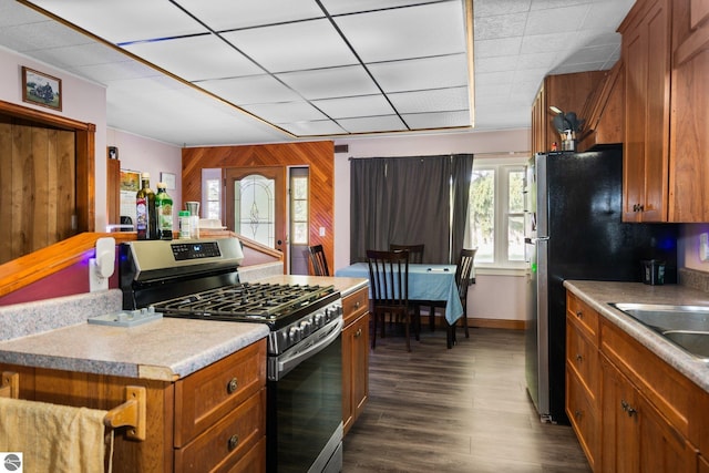 8817 Wilson Rd, Buckley, MI 49620 - kitchen with stainless steel gas range oven, wooden walls, brown cabinets, dark wood-style floors, and light countertops