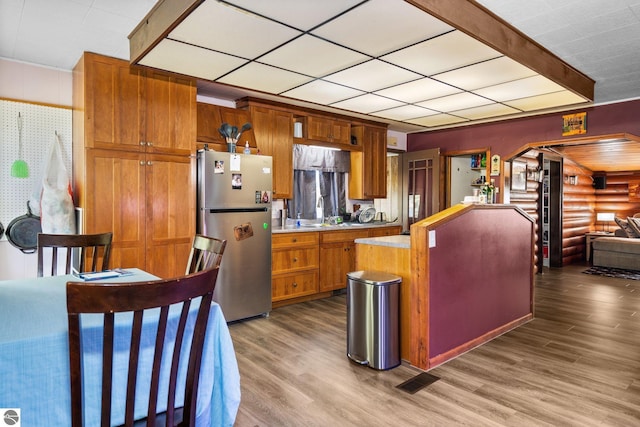 8817 Wilson Rd, Buckley, MI 49620 - kitchen featuring freestanding refrigerator, light countertops, wood finished floors, brown cabinets, and log walls