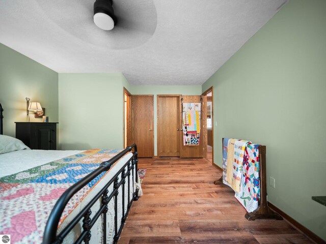 6307 Summit Ct, Traverse City, MI 49686 - bedroom with light wood-type flooring, a ceiling fan, two closets, a textured ceiling, and baseboards