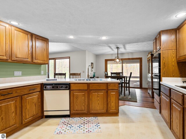 6307 Summit Ct, Traverse City, MI 49686 - kitchen with white dishwasher, a peninsula, a sink, brown cabinetry, and recessed lighting