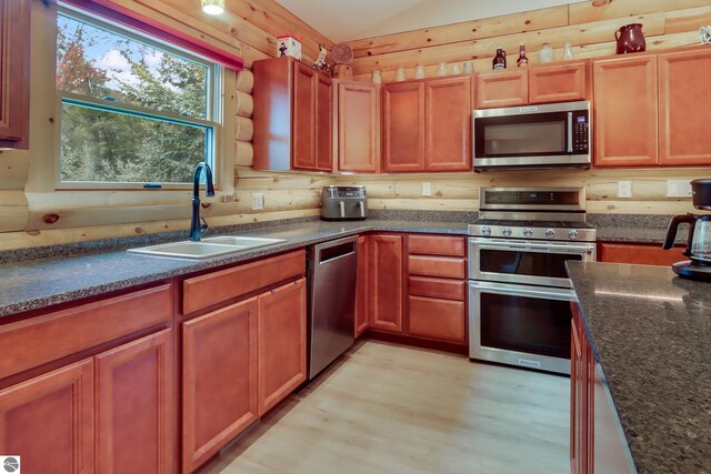 kitchen featuring stainless steel appliances, a sink, light wood-type flooring, and dark stone counters