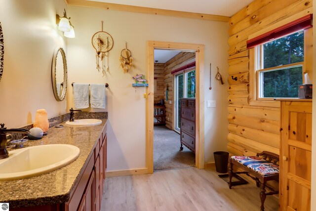 bathroom with wood finished floors, double vanity, rustic walls, and baseboards
