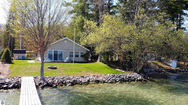 10701 SW Torch Lake Dr, Rapid City, MI 49676 - rear view of house with a lawn, a water view, and an outdoor fire pit