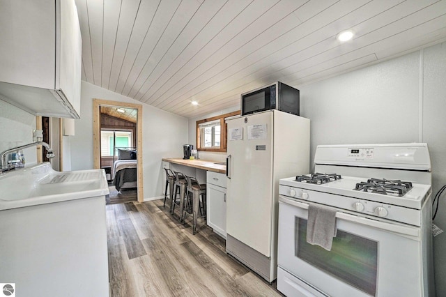 kitchen featuring white appliances, vaulted ceiling, light wood-style flooring, light countertops, and white cabinets