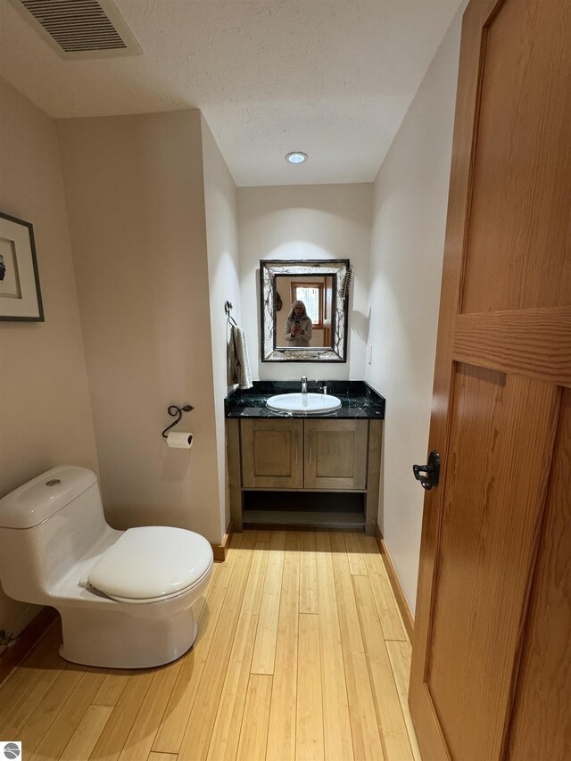 bathroom with toilet, vanity, wood-type flooring, and baseboards