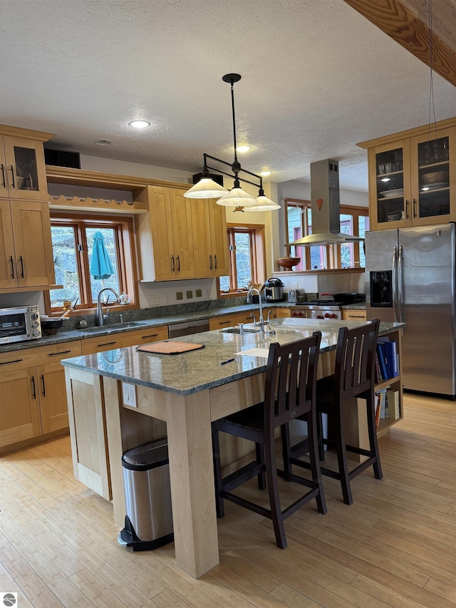 kitchen with island exhaust hood, appliances with stainless steel finishes, a sink, a textured ceiling, and a kitchen island with sink