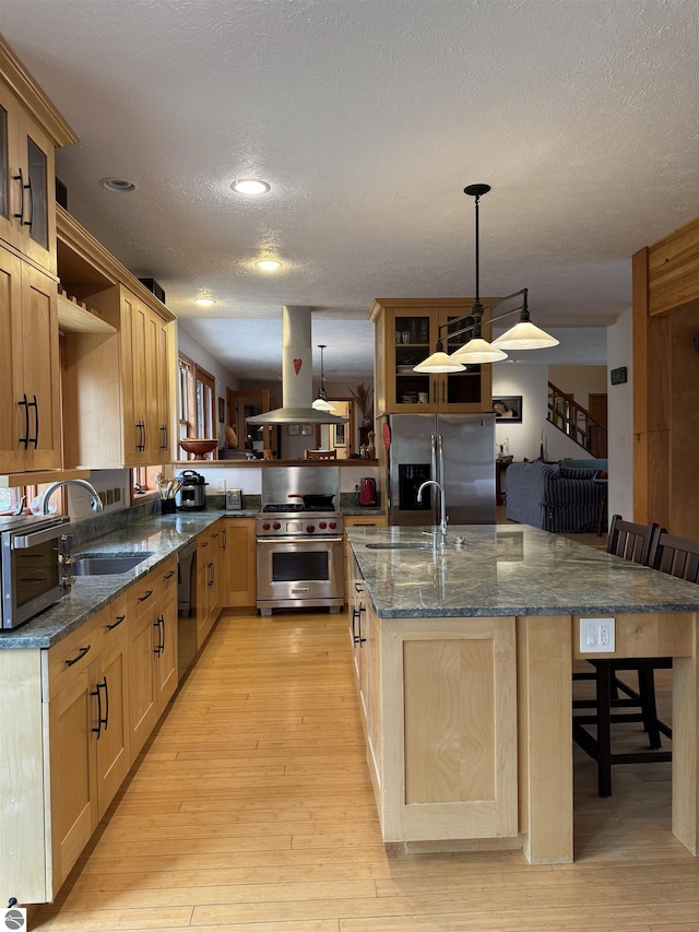 kitchen featuring appliances with stainless steel finishes, island exhaust hood, open shelves, a sink, and a breakfast bar