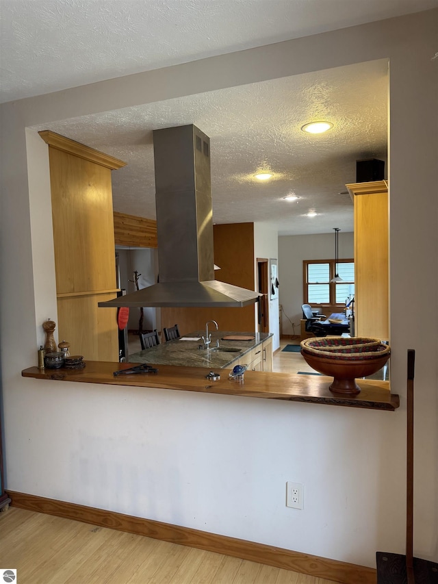 kitchen featuring range hood, wood finished floors, a textured ceiling, baseboards, and a sink