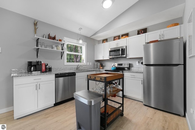 kitchen with appliances with stainless steel finishes, lofted ceiling, light wood-style floors, white cabinetry, and a sink
