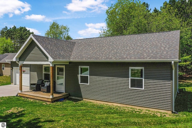rear view of house featuring an attached garage, a shingled roof, driveway, and a lawn