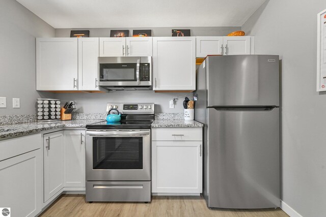 kitchen with appliances with stainless steel finishes, light wood-style flooring, white cabinetry, and light stone countertops
