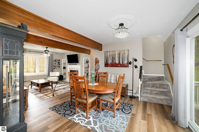 4480 Mockingbird Cir, Farwell, MI 48622 - dining area featuring a fireplace, light wood-type flooring, stairs, ceiling fan, and beam ceiling