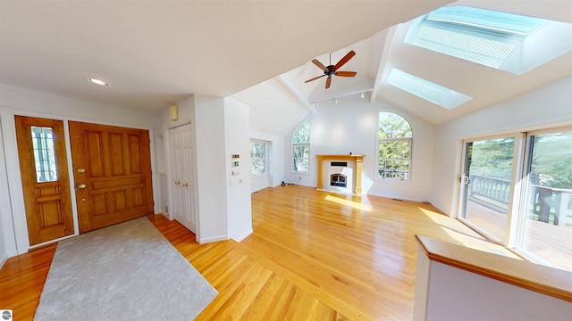 foyer entrance featuring light wood-style floors, ceiling fan, lofted ceiling, a skylight, and a fireplace with flush hearth