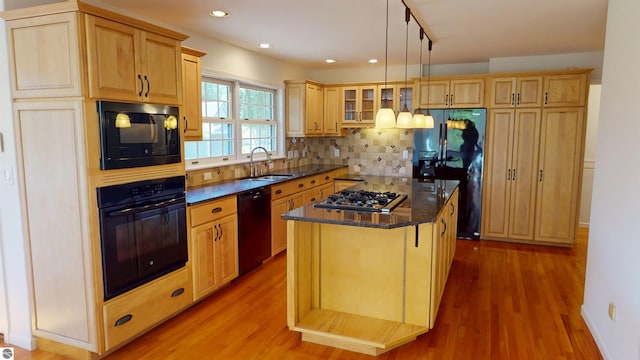 kitchen with black appliances, a sink, a center island, light wood-style flooring, and backsplash
