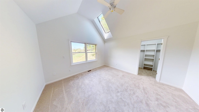 unfurnished bedroom with a skylight, carpet flooring, a walk in closet, a ceiling fan, and baseboards