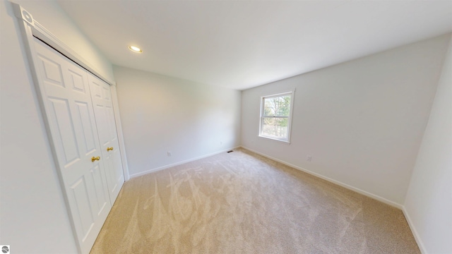 unfurnished bedroom featuring light colored carpet, baseboards, recessed lighting, and a closet
