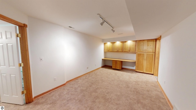 interior space featuring rail lighting, baseboards, and light colored carpet