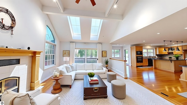living room featuring a tile fireplace, light wood finished floors, beam ceiling, a skylight, and high vaulted ceiling