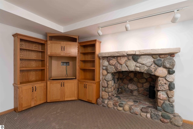 unfurnished living room with track lighting, dark carpet, a stone fireplace, and baseboards