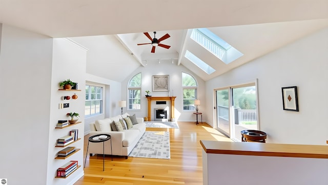 living room with ceiling fan, light wood-style floors, a skylight, a fireplace, and track lighting