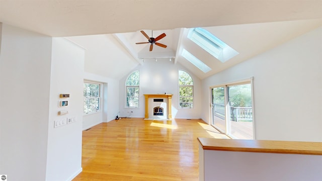 unfurnished living room with a skylight, ceiling fan, beamed ceiling, light wood-style floors, and a fireplace with flush hearth