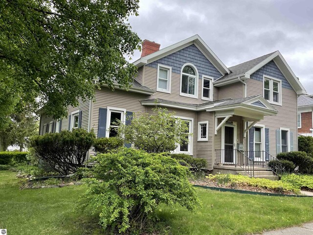 630 N State St, Alma, MI 48801 - view of front of property featuring a chimney, a front yard, and a shingled roof