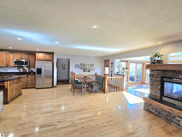 205 S Elm St, Suttons Bay, MI 49682 - kitchen featuring appliances with stainless steel finishes, dark countertops, brown cabinetry, light wood finished floors, and a stone fireplace