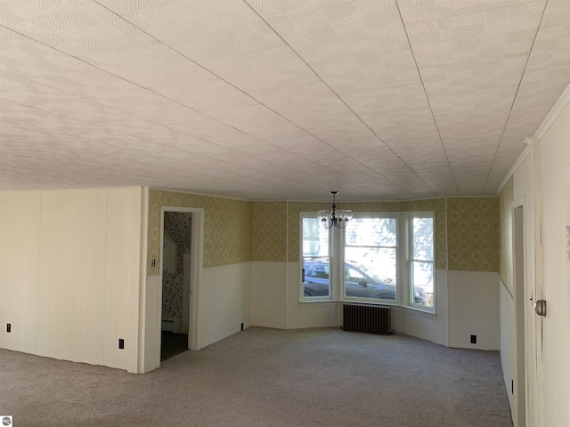 empty room with radiator heating unit, wallpapered walls, carpet floors, a wainscoted wall, and a chandelier